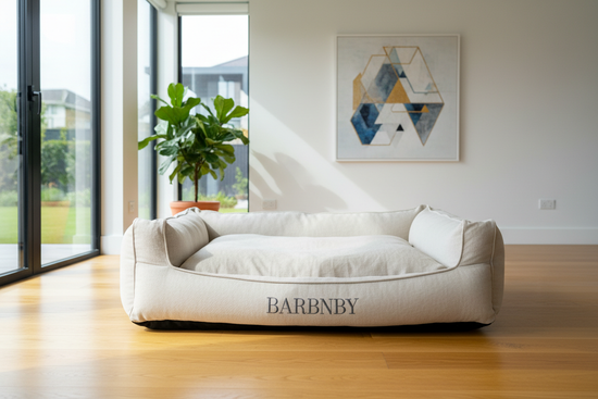 dog bed on the floor with the dog's name on it in a well lit modern room with white walls, yellow wood floors and a lot of natural light